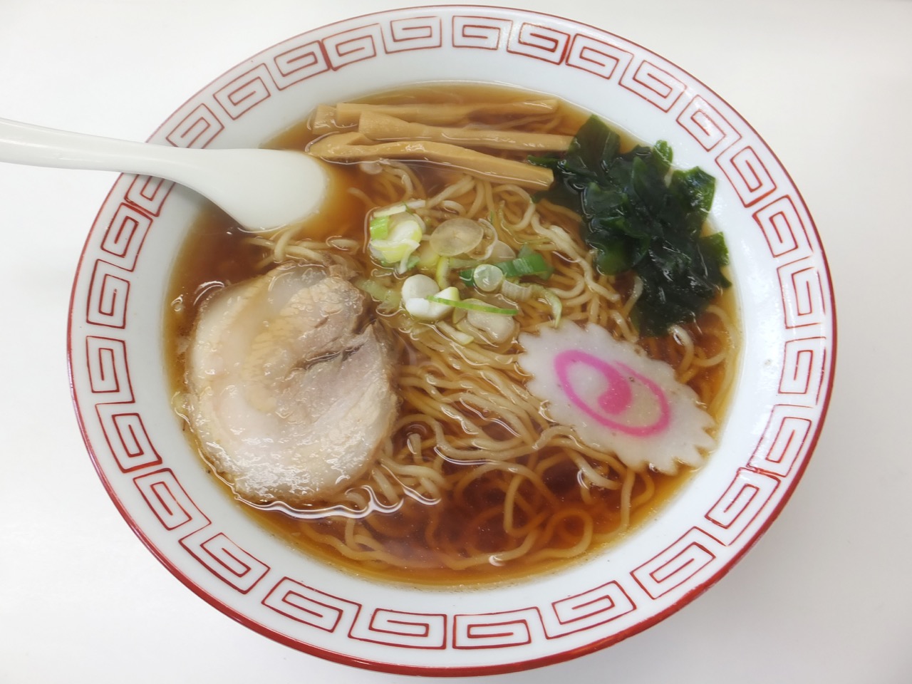 A bowl of shoyu ramen with clear brown broth, chashu, and green onions
